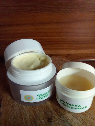 Zwei Behälter mit Pflegecreme, einer geöffnet und einer geschlossen, auf einem Holzuntergrund.