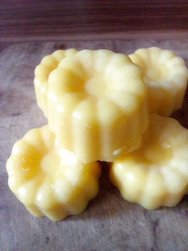 Vier gelbe, gewellte Puddingförmchen auf einer Holzoberfläche.