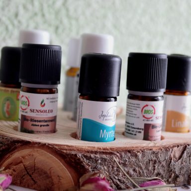 Ätherische Öle in kleinen Fläschchen auf einem runden Holzuntersetzer.