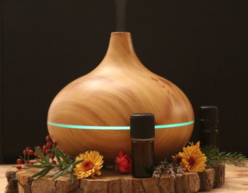 Holzfarbener diffuser mit blauem Licht, umgeben von ätherischen Ölen und Blumen.