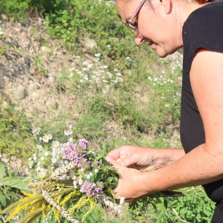 Frau mit Blumen im Feld, umgeben von hohen Gräsern und Blumen.