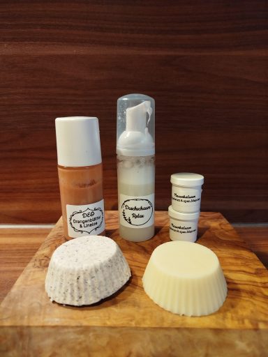 Zwei Flaschen Pflegeprodukte und drei feste Seifen auf einem Holzbrett angeordnet.