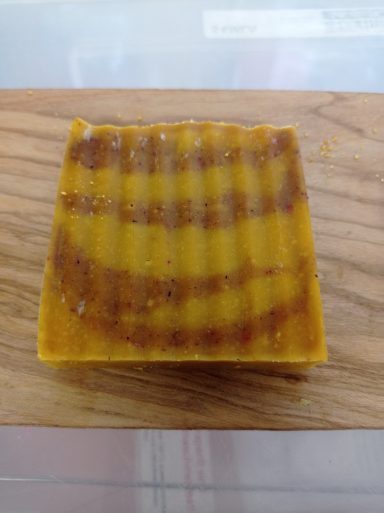 Ein kleines Stück gelber Seife mit einer gestreiften Oberfläche auf einem Holzbrett.