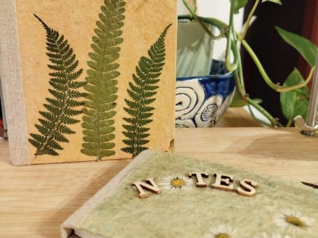 Sechs rosa Kerzen mit gepressten Blumenmotiven auf einem Holzuntergrund.