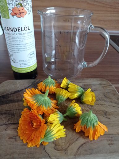 Ein Holzbrett mit orangefarbenen Ringelblumen und einem Glasbehälter daneben.