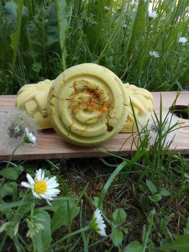 Gelbe Seife in spiralförmiger Form, auf Holzplatte im Gras mit Blumenarrangement.